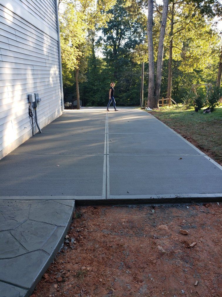 Concrete walkway beside a white building, leading to a person in the distance among trees.