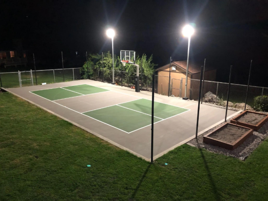 “Lighted outdoor sport court glowing at night with green and gray playing areas after a court builder service in Henderson, NV”