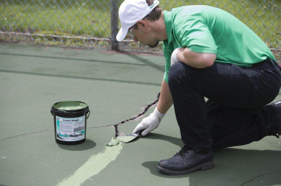 “Technician repairing cracks on a green sport court surface with sealant during a court builder service in Henderson, NV”