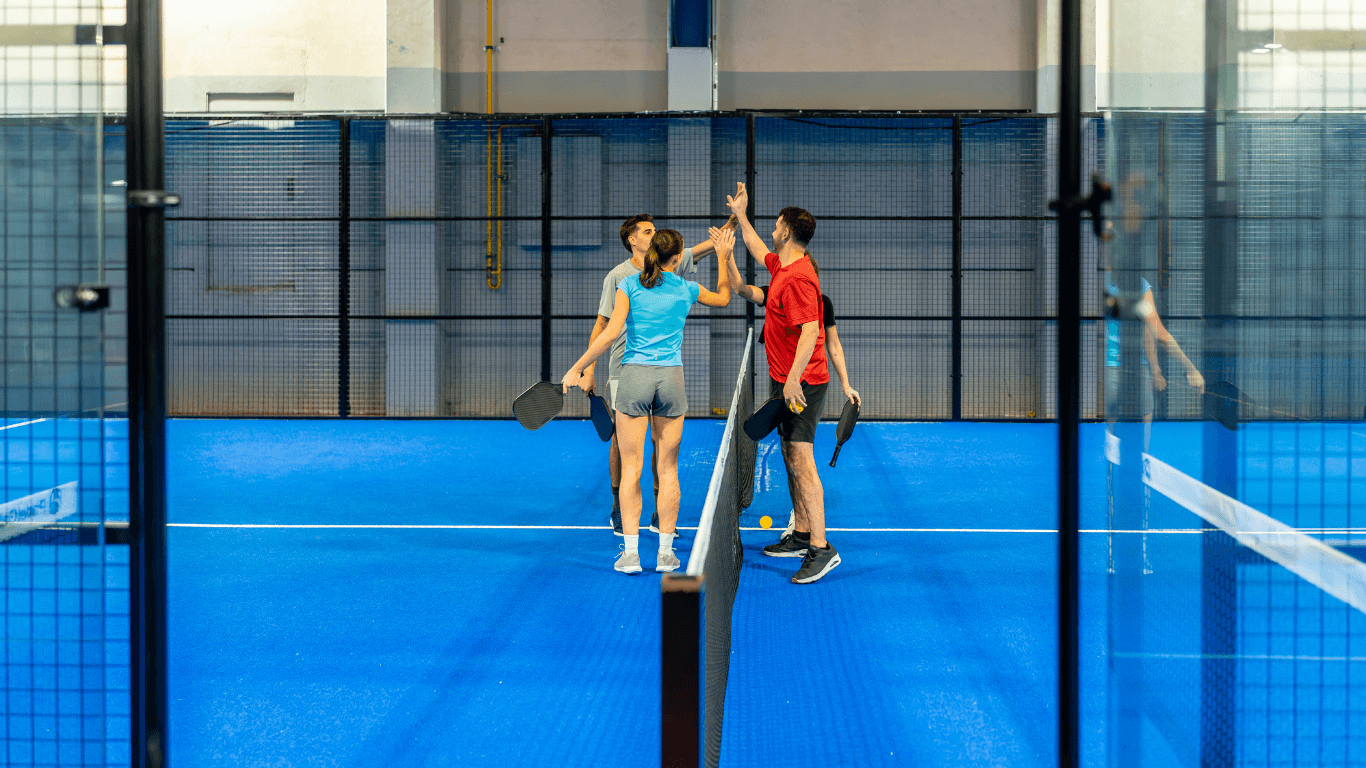 “Players standing on a bright blue indoor pickleball court with glass walls after a court builder service in Henderson, NV”