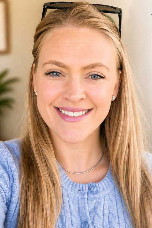 Woman with long brown hair smiling, wearing a black blazer and gray shirt, against a gray backdrop.