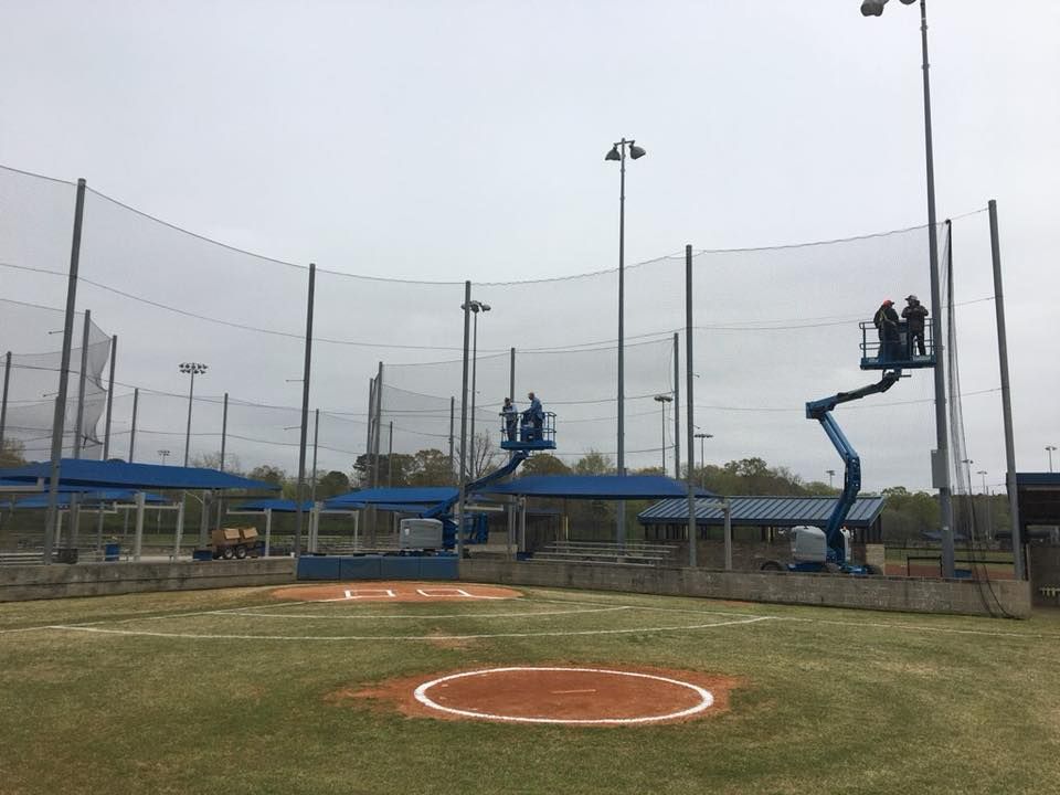 Baseball field with two elevated maintenance lifts beside the outfield netting on an overcast day