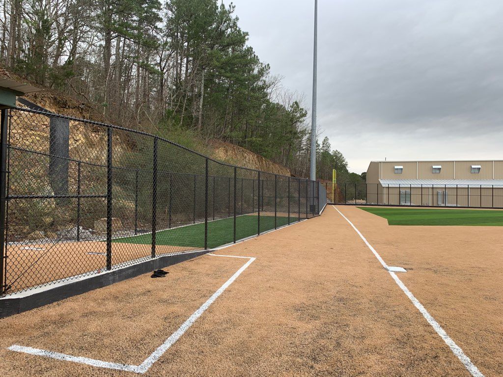Empty baseball field with dirt baselines, black fence, and cloudy sky