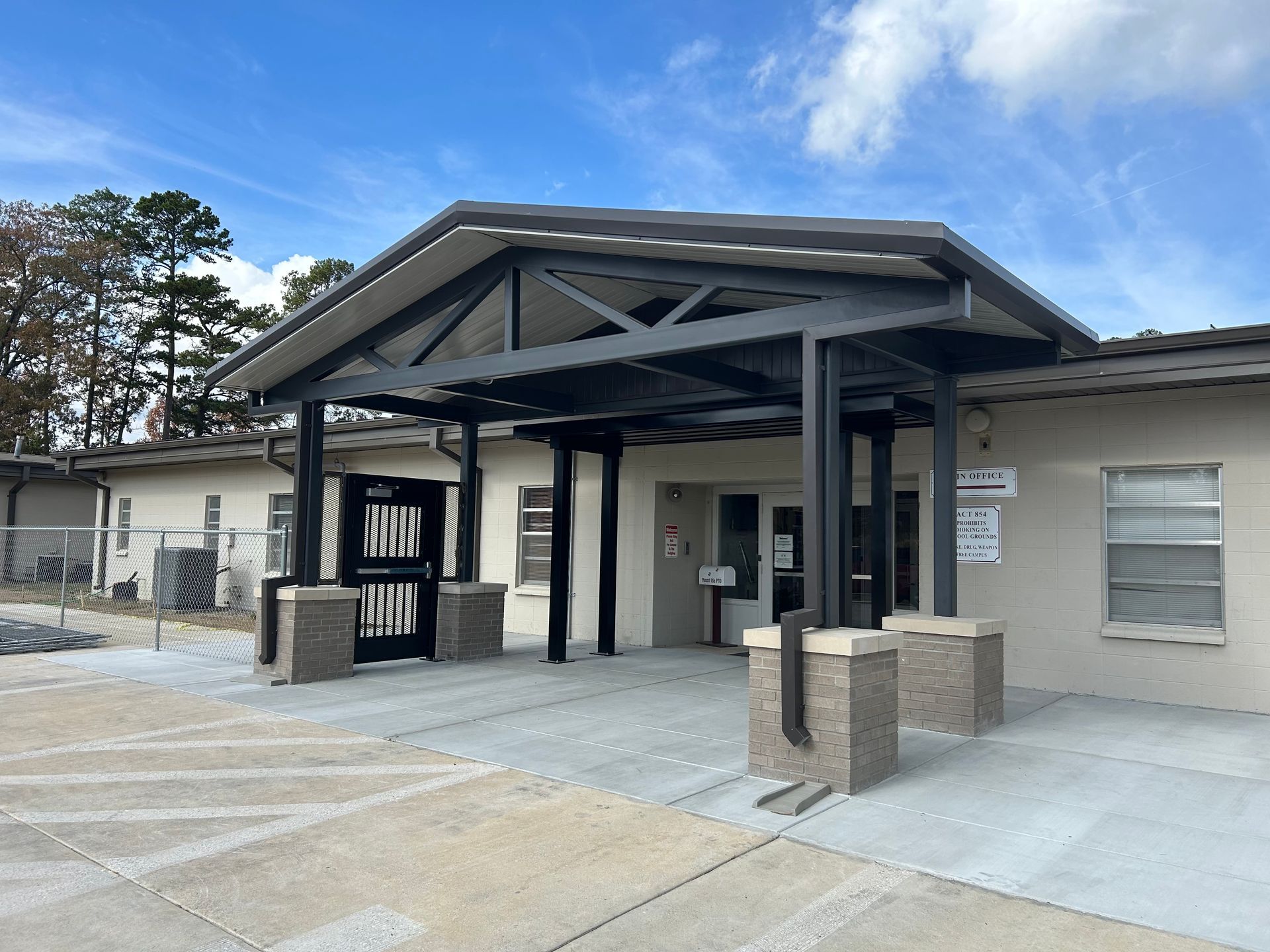 Building entrance with a covered canopy, concrete walkway, and beige exterior walls.