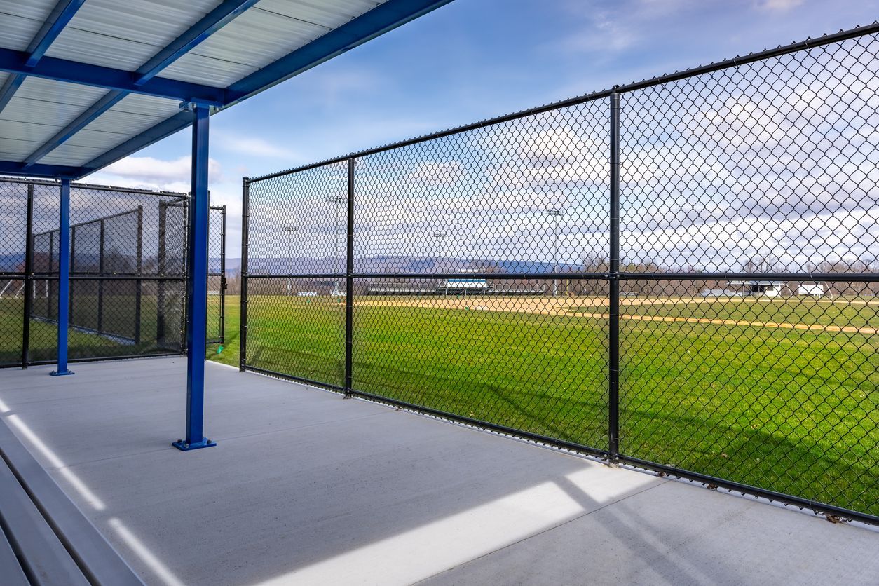 Empty covered walkway beside a chain-link fence overlooking a green field and distant water