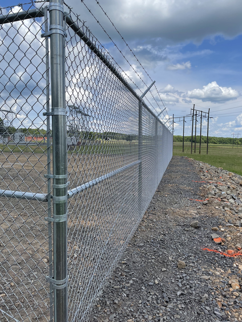 Chain-link fence along a gravel roadside under a cloudy sky.