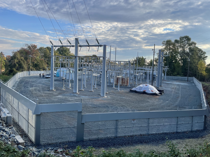 Construction site with steel utility framework and concrete foundation on a gravel lot at dusk