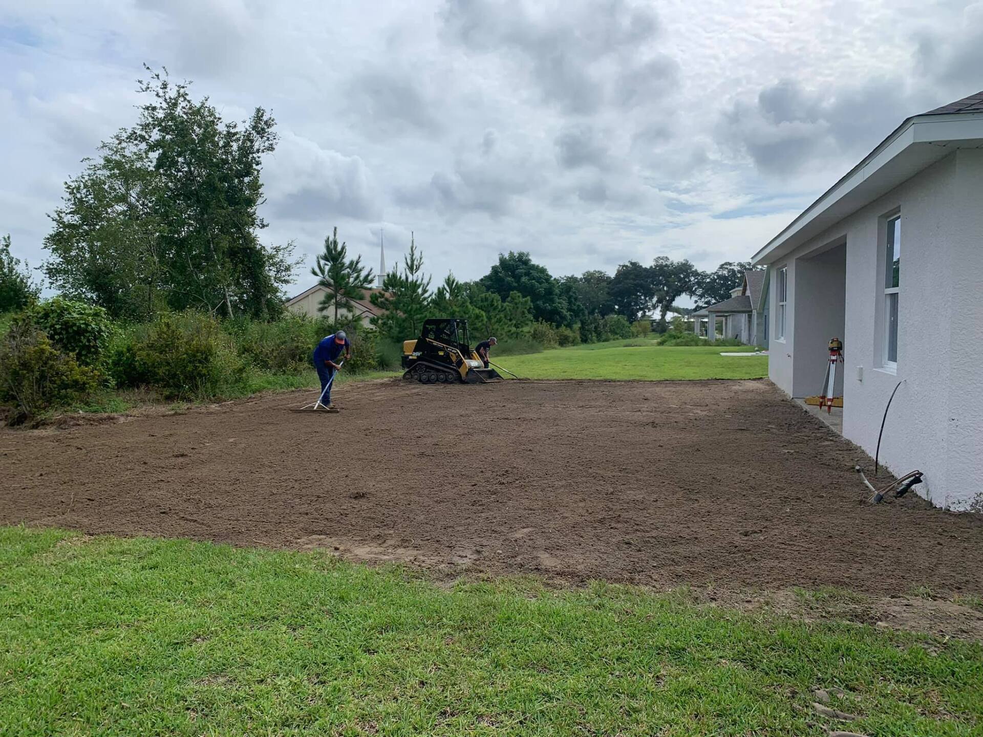 Dump truck services with person raking soil on Ocala, FL property