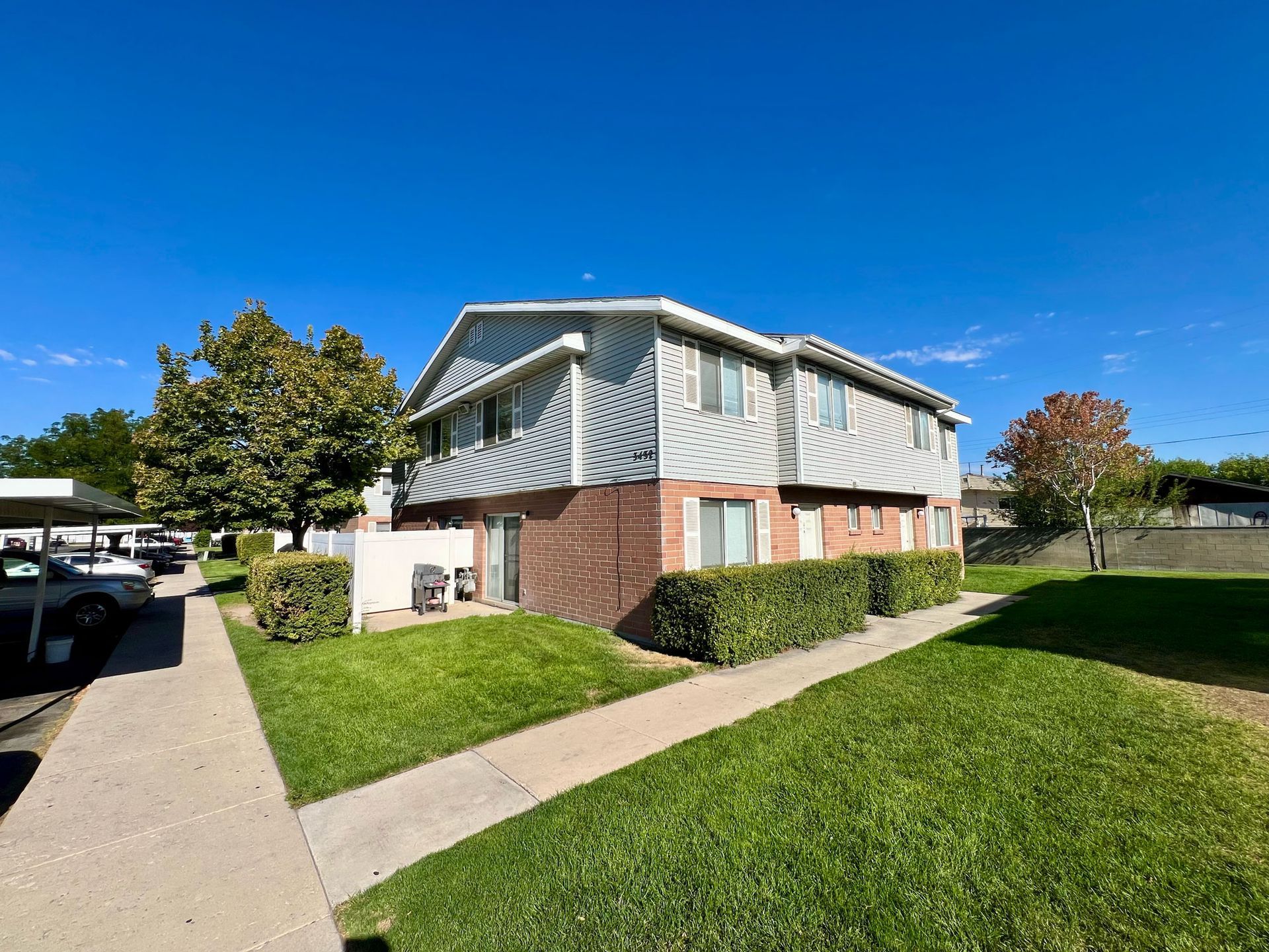 Two-story apartment building with brick base, silver siding, and green lawn on a sunny day.