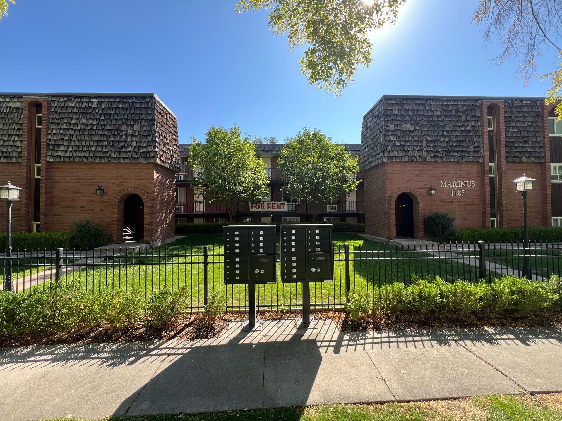Apartment building with brick exterior, mailboxes in foreground, sunny day.