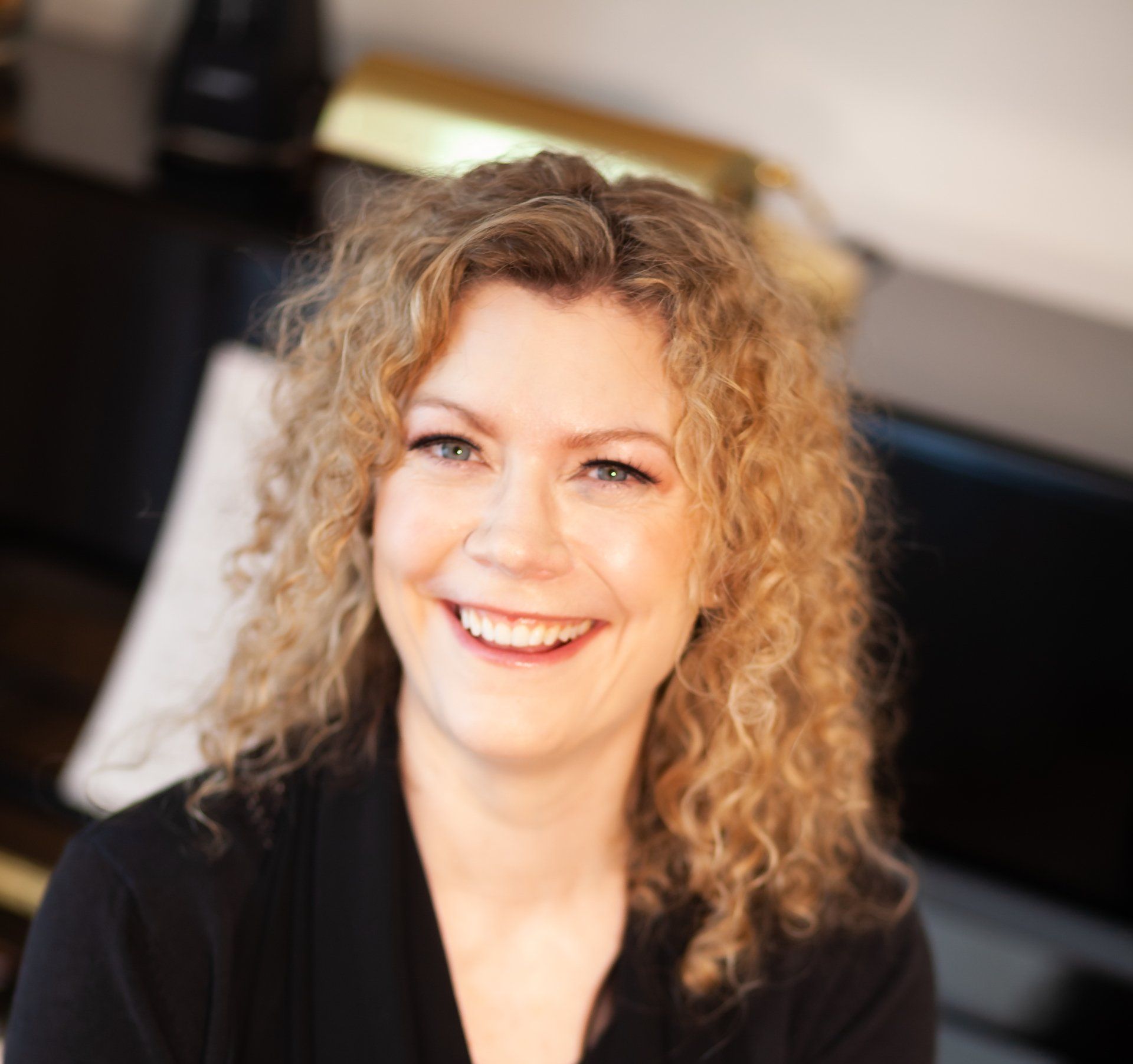 A woman with curly hair is smiling and wearing a black shirt
