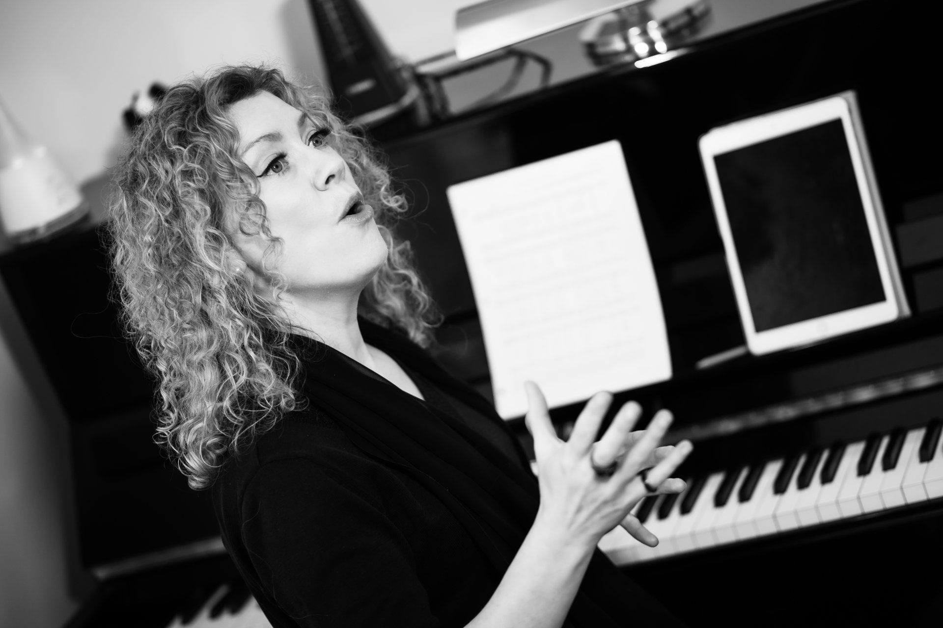A woman is singing in front of a piano in a black and white photo.