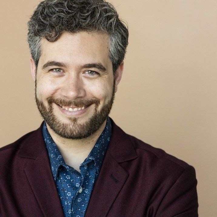 A man with a beard wearing a maroon jacket and a blue shirt