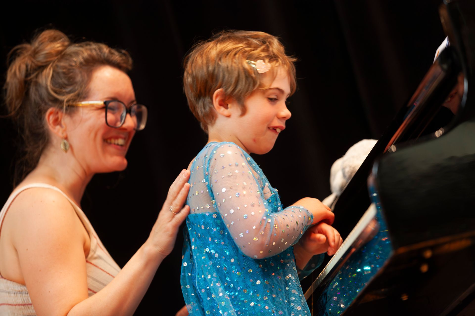 A woman is helping a little girl play a piano.