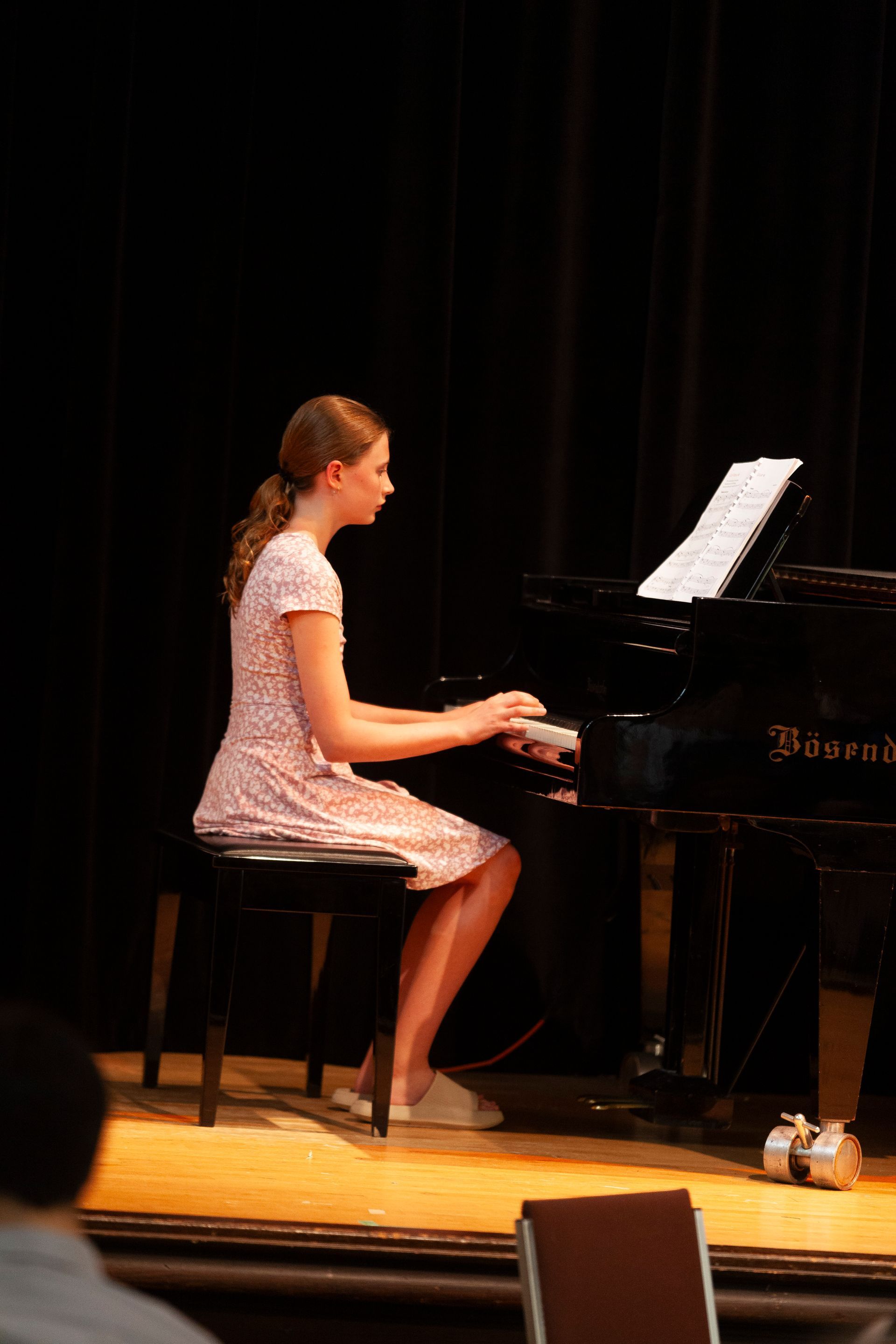 A young girl is sitting on a stool playing a piano on a stage.