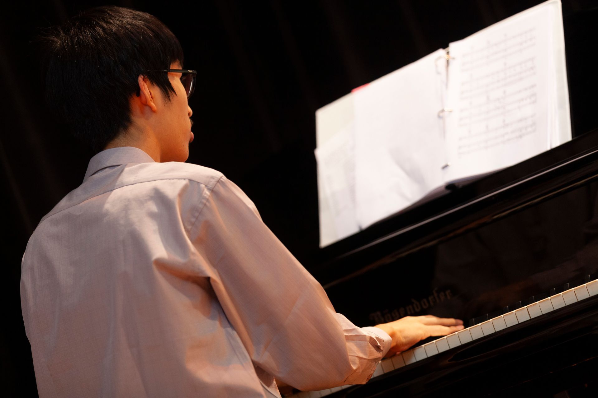 A man in a pink shirt is playing a piano