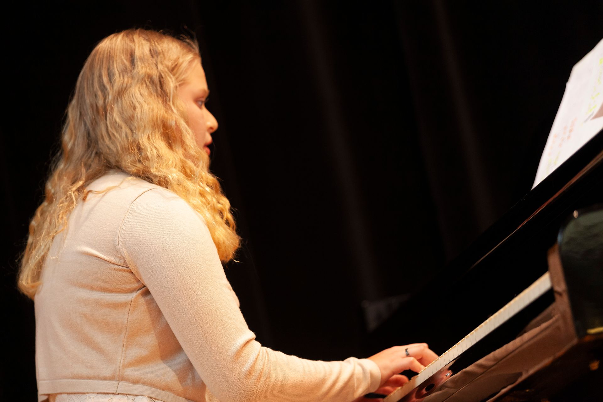 A young girl is playing a piano on a stage.