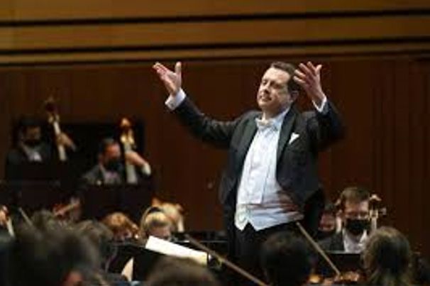 A man in a tuxedo is leading an orchestra on a stage.