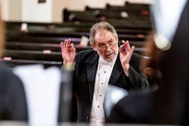 A man in a tuxedo is leading an orchestra in a church.