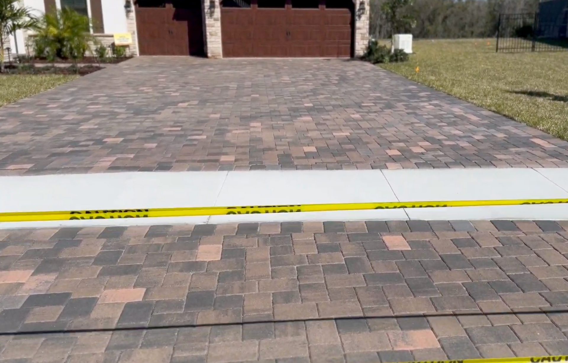 A patterned paver driveway featuring multi-toned blocks, separated by a concrete walkway blocked by yellow caution tape.