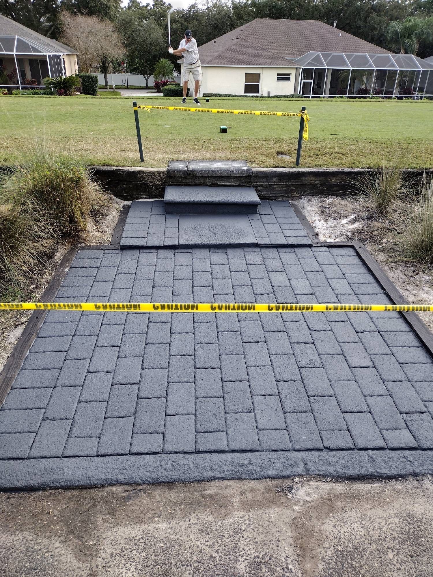 Newly installed dark gray brick pavers lead to stone steps in a grassy backyard, blocked by yellow caution tape.