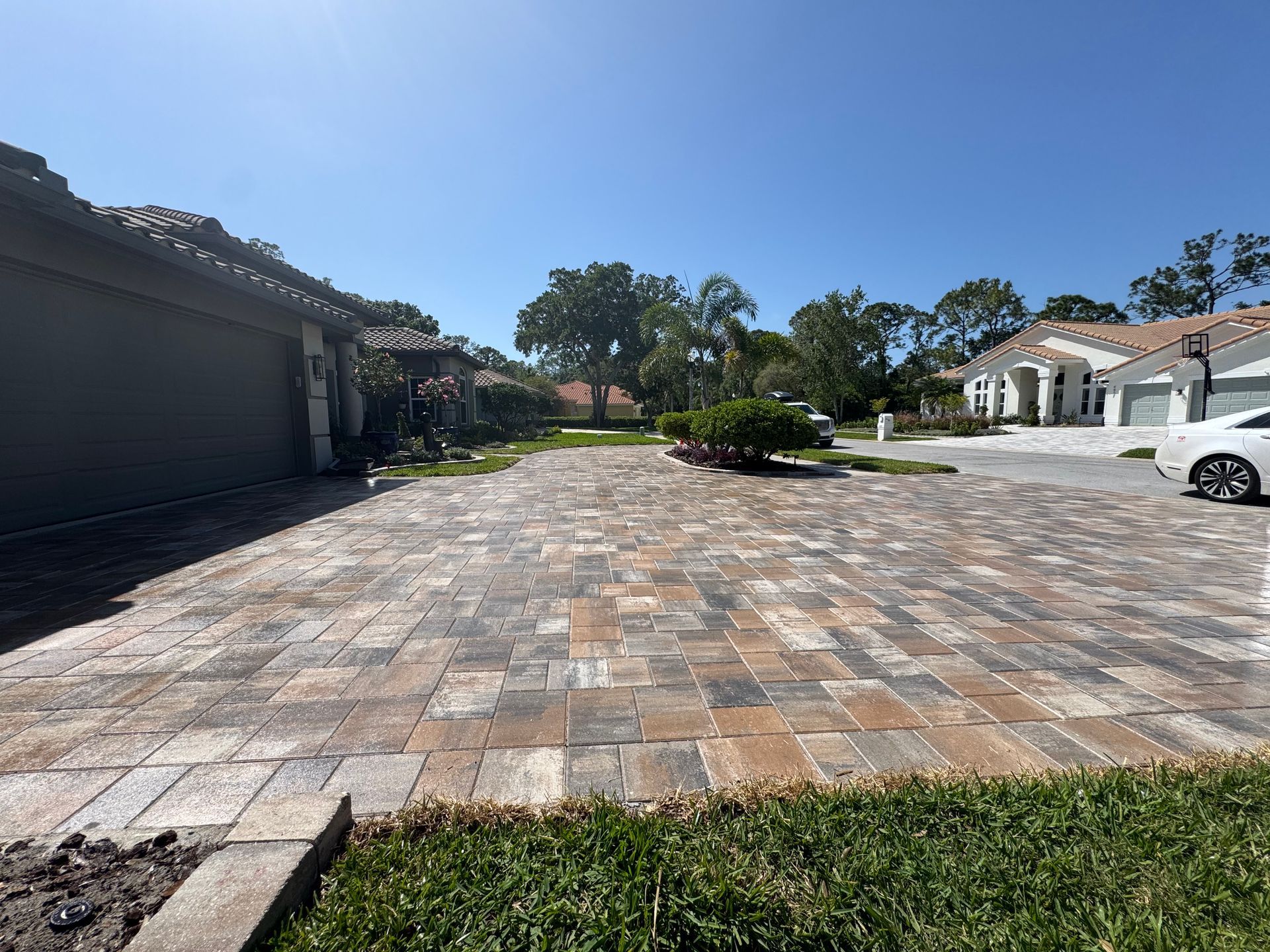 A wide driveway paved with rectangular stones in mixed shades of gray, tan, and brown, leading up to a suburban home.