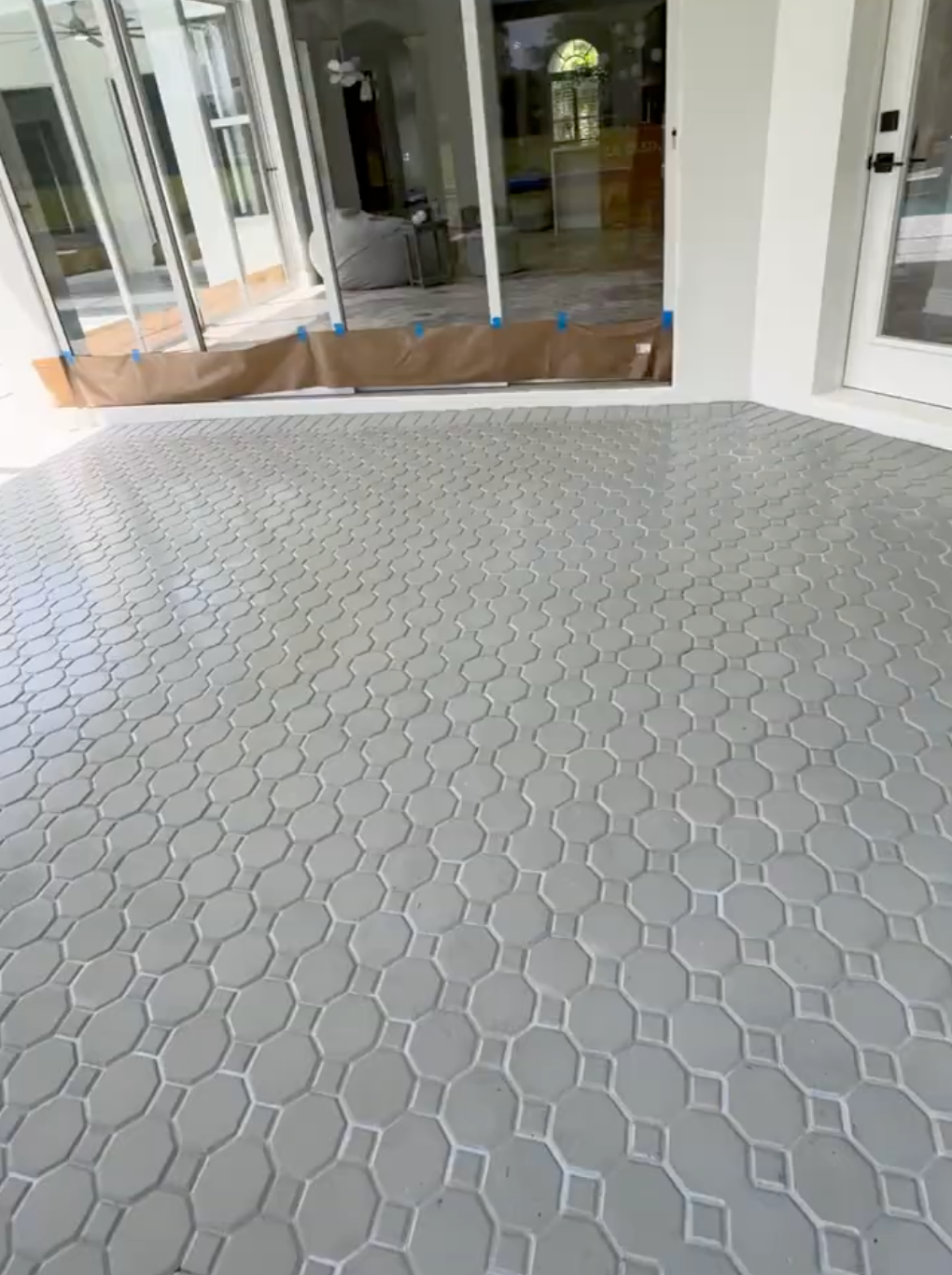 A patio floor covered in light gray, octagon-patterned tile, positioned in front of a house with sliding glass doors.