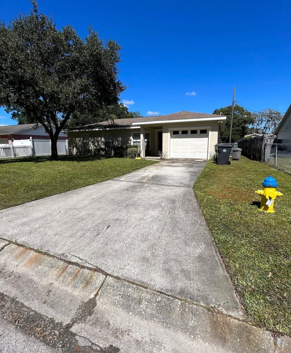 A driveway paved with light gray rectangular stones featuring a discolored patch in the center and a red hose nearby.