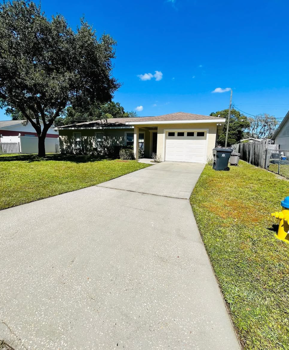 A taupe two-story house with a paved driveway, featuring a yellow caution tape stretched across the lower section.