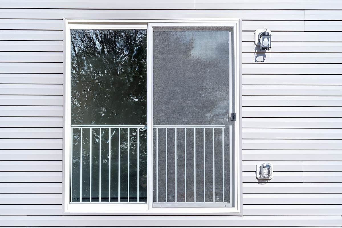 A White House With a Sliding Glass Door and a Balcony — Manning Blinds & Awnings in Old Bar, NSW