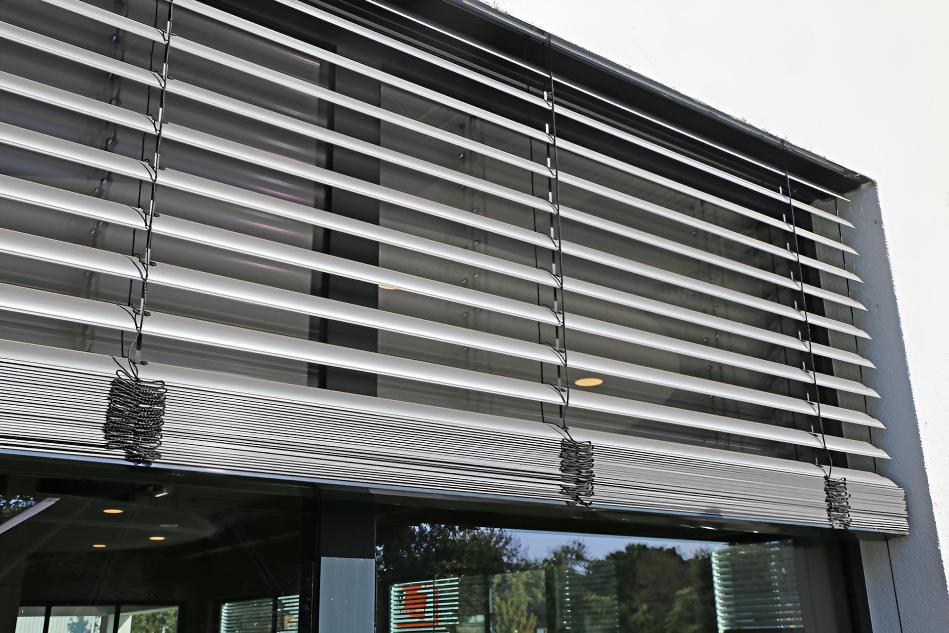 Exterior view of building with horizontal, adjustable sun shades over a large window — Manning Blinds & Awnings in Taree, NSW