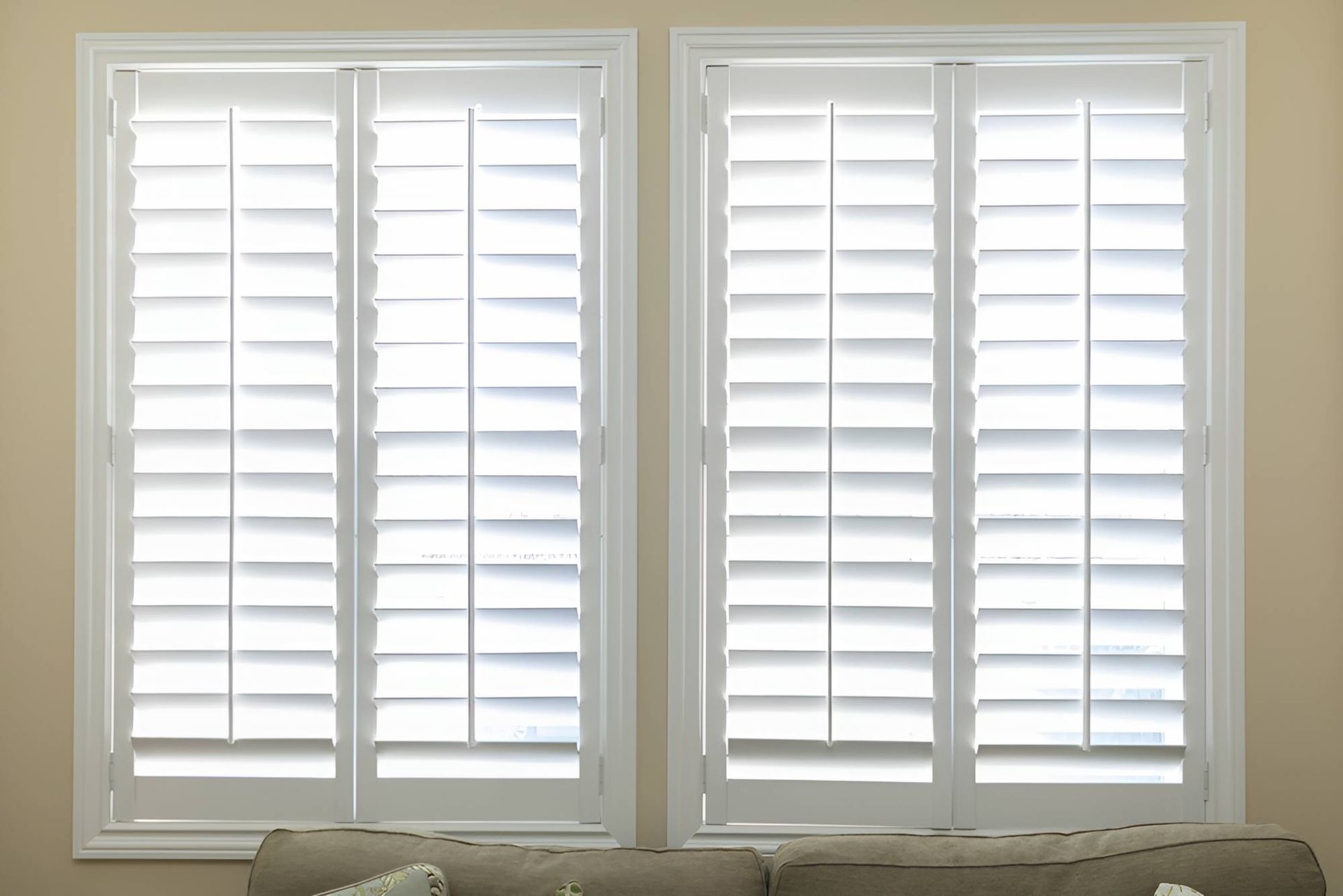A Living Room With Two Windows With White Shutters and a Couch — Manning Blinds & Awnings in Taree, NSW