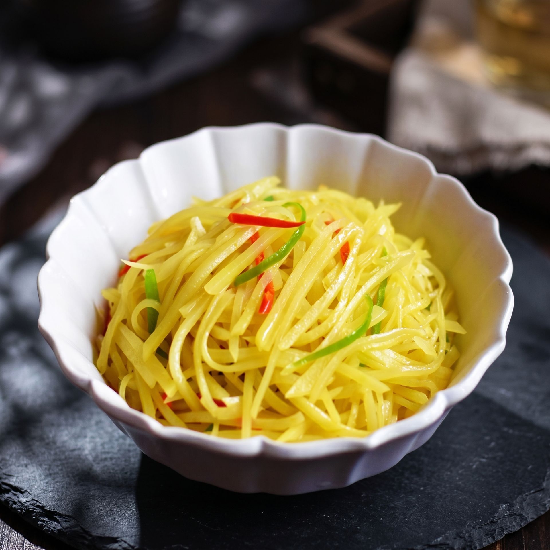 White bowl of yellow shredded salad garnished with red and green chilies on a dark slate plate