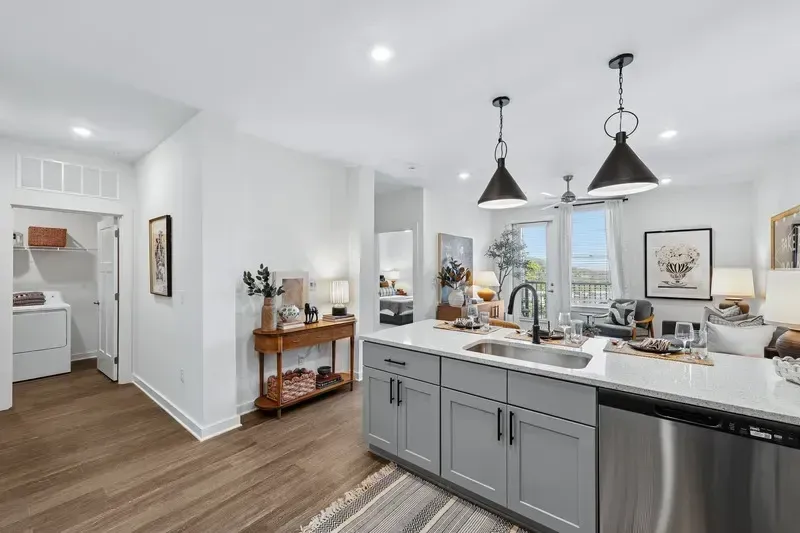Modern kitchen with gray cabinets, island, sink, dishwasher, and adjacent living area with a view.
