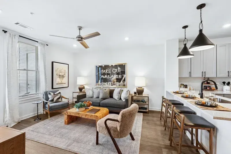 Modern living room and kitchen area with gray sofa, abstract art, and kitchen island with bar stools.