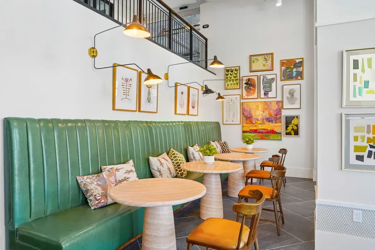 Seating area with green banquette, round tables, and artwork.