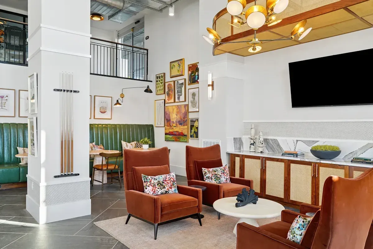 Modern community lounge with orange armchairs, a large TV, green booth seating, and a billiards cue rack.