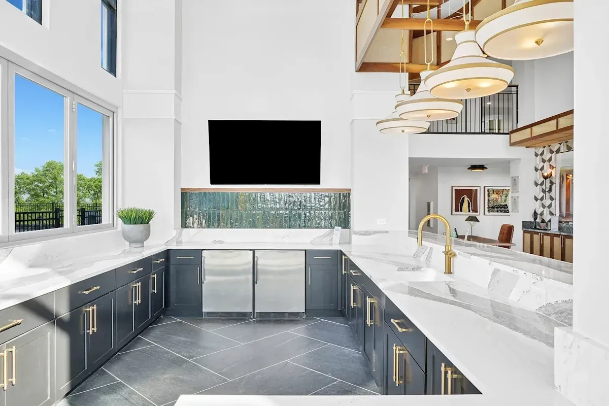 Modern kitchen area with dark cabinets, marble countertops, stainless steel appliances, and a large window.