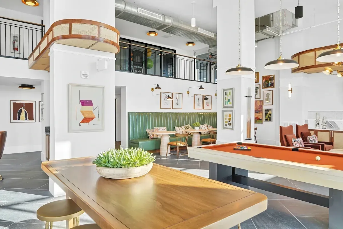 Interior of a modern community lounge with a pool table, green booths, and dining tables.