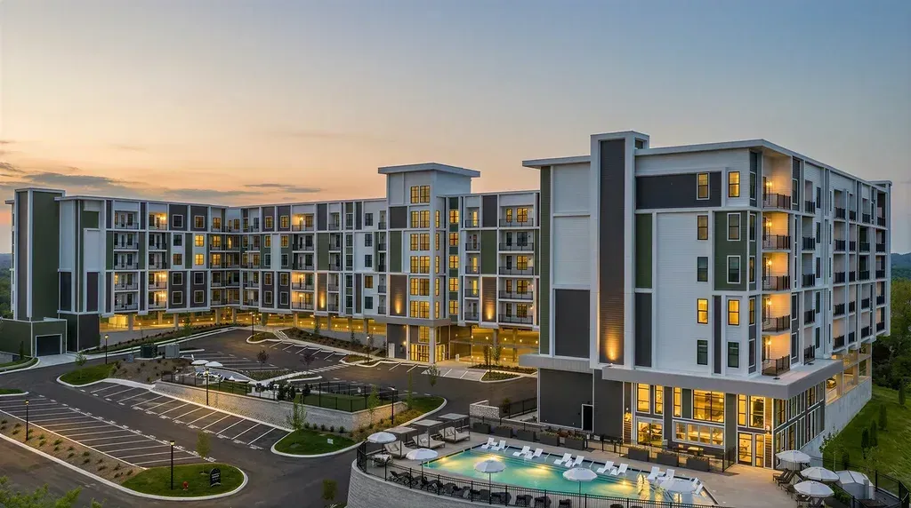Luxury apartment building with pool and parking lot at dusk.