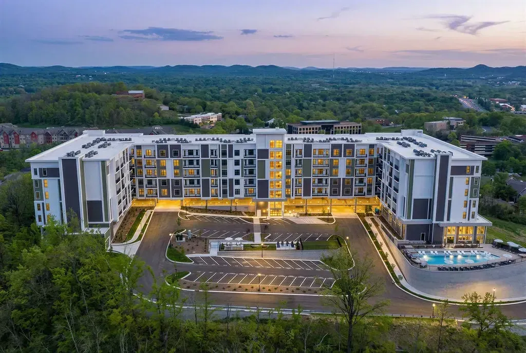 Exterior view of a modern apartment building with a pool and surrounding landscape.