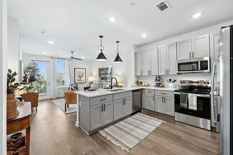 Bright modern kitchen with gray island, white cabinets, stainless appliances, and wood floors.