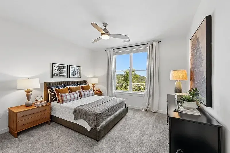 Bright bedroom with a bed, nightstands, ceiling fan, and window with curtains.