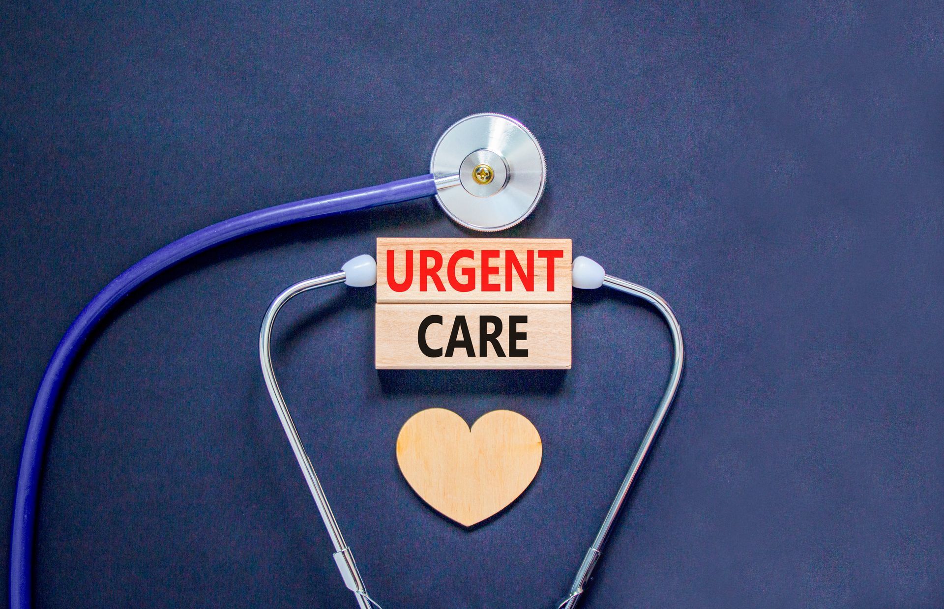 Stethoscope arranged around a wooden heart and urgent care sign on a dark background.