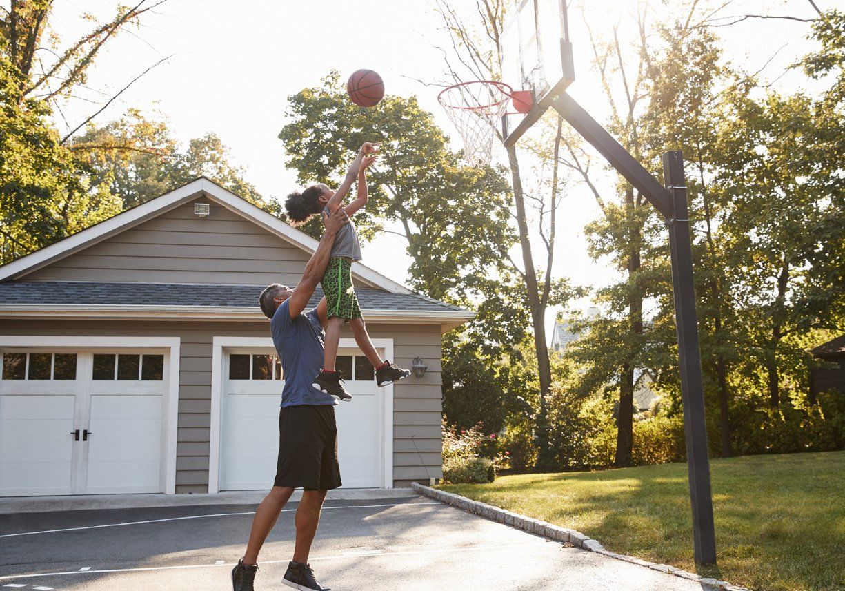 A man and a child are playing basketball in front of a garage.