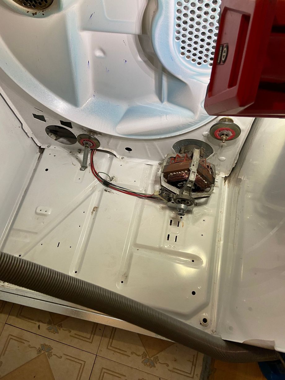 Burned wiring and damaged components inside the bottom of a white appliance, with soot and melted plastic