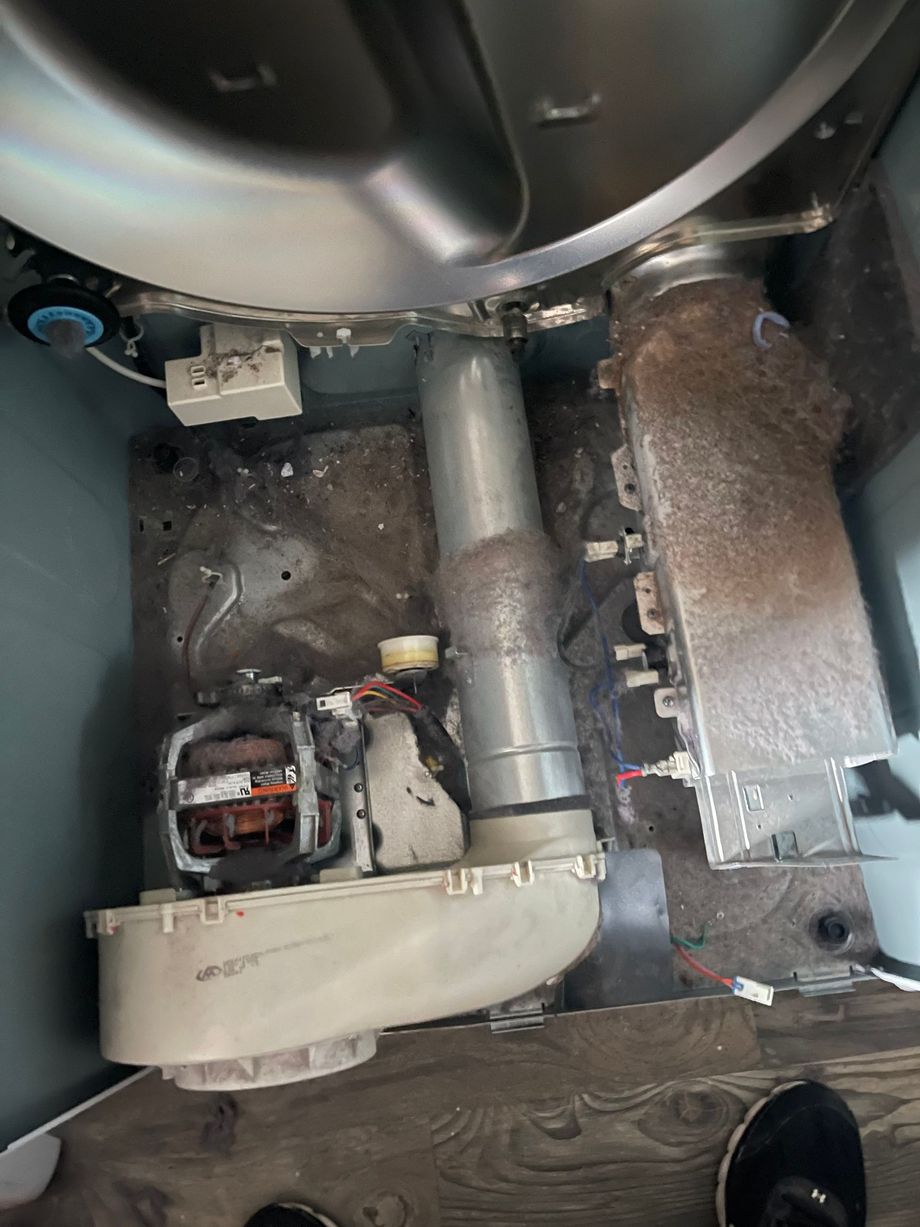 Interior of a car engine bay with exposed components, hoses, and a large circular fan housing.