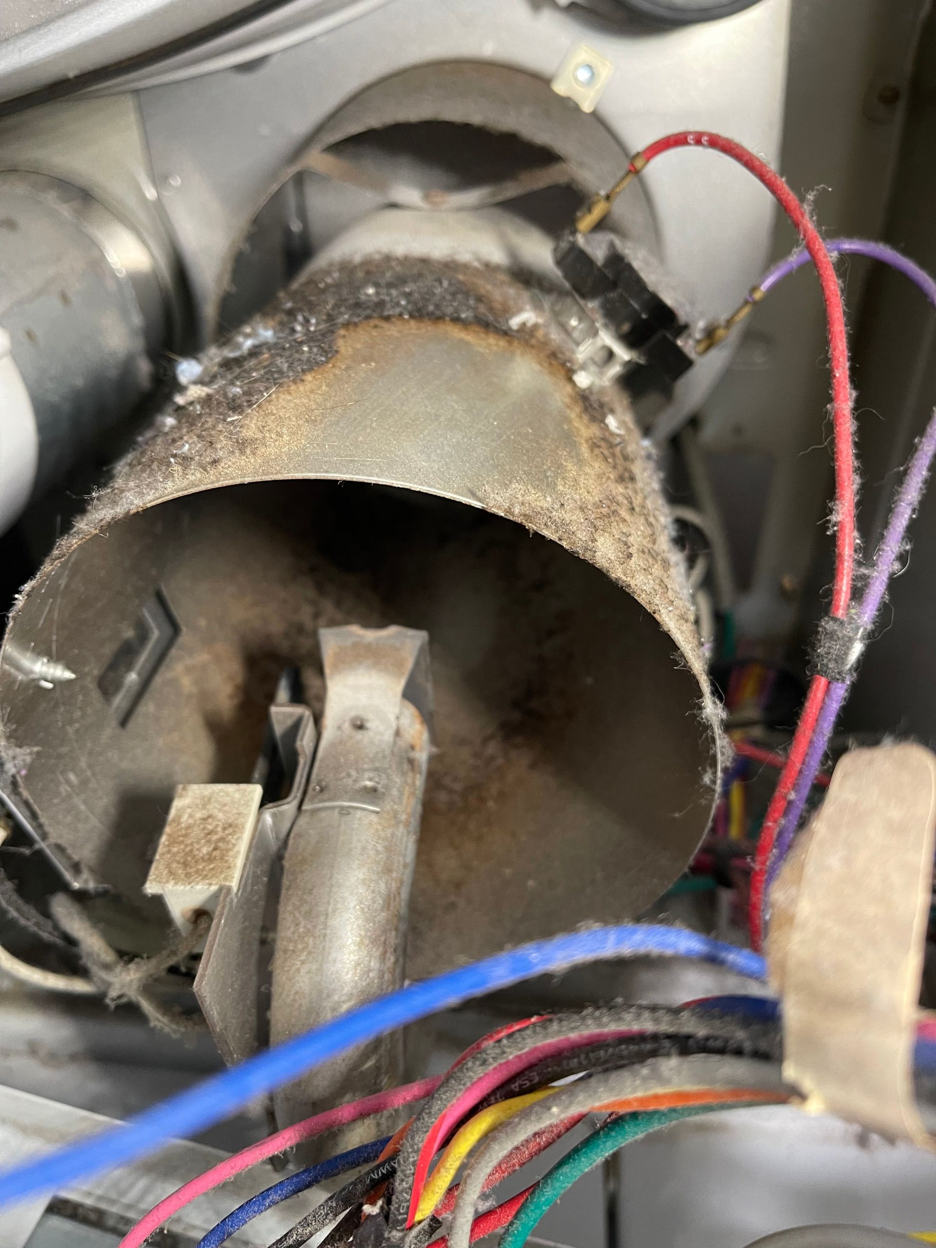 Close-up of a rusty metal duct or pipe with exposed wires inside a mechanical compartment