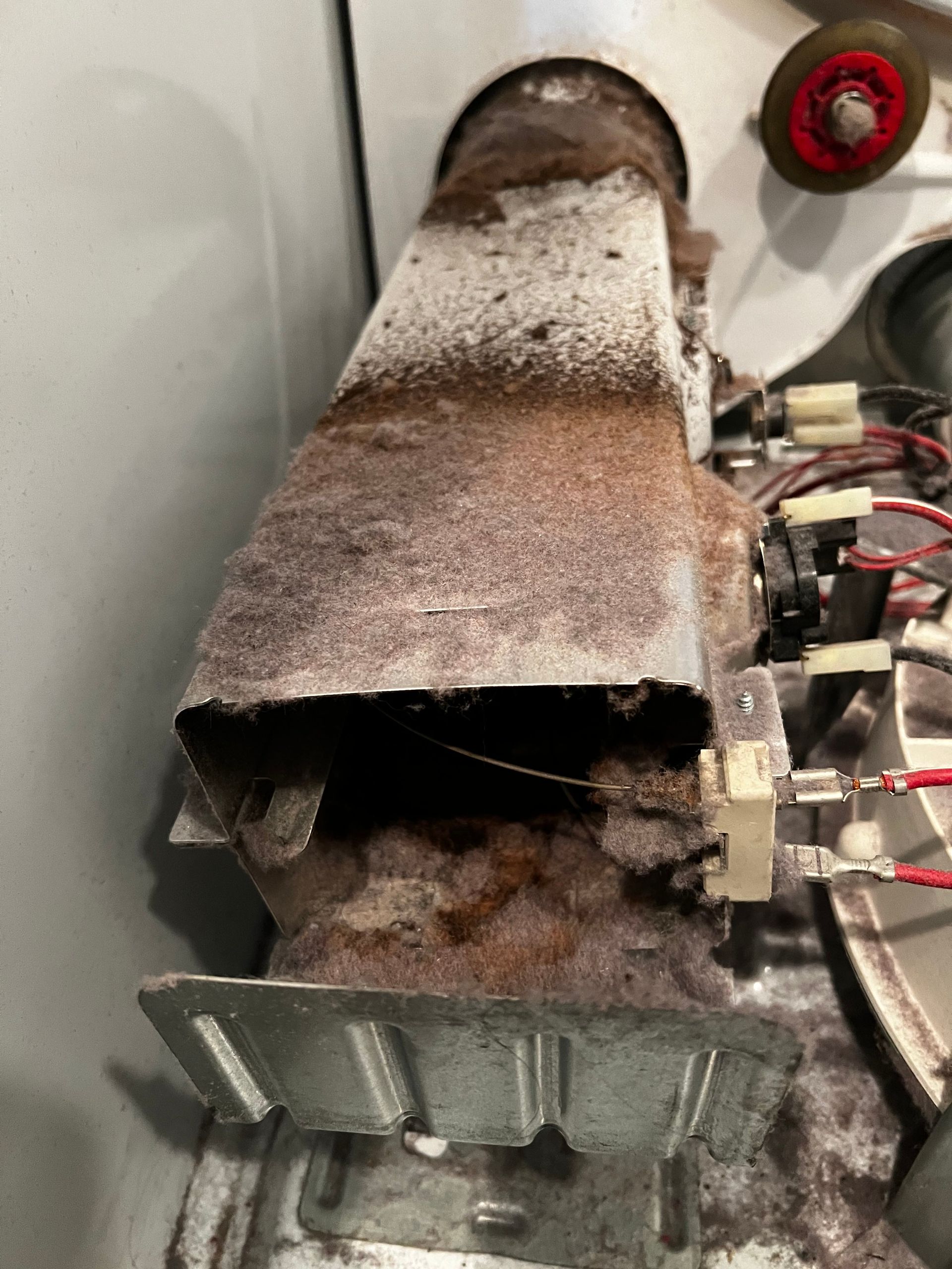 Rusty damaged metal duct with a hole and wiring inside, coated in white dust or frost.