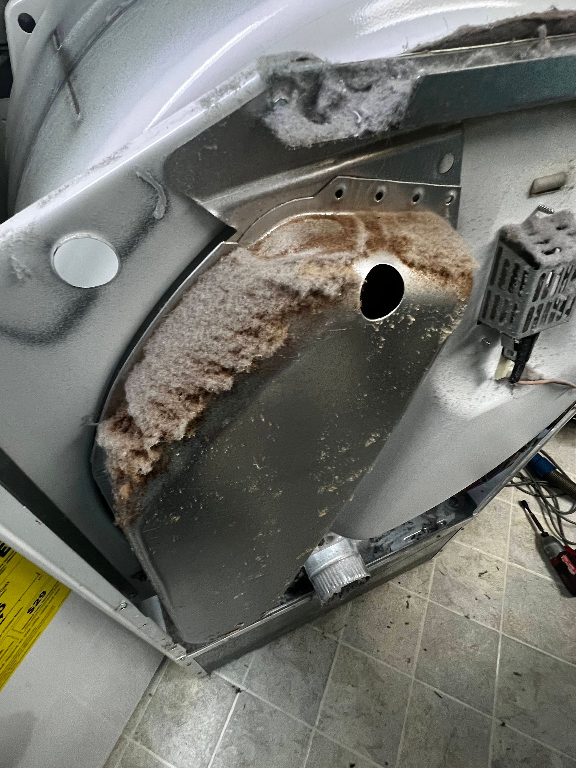 Rust-damaged metal panel inside industrial equipment, with a large circular hole and peeling corrosion.